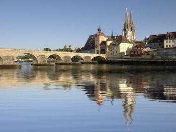 Arch bridge over river by building against clear sky