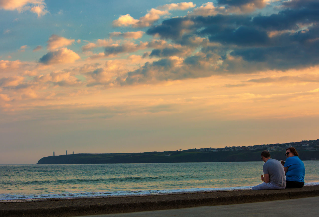 PEOPLE SITTING AT BEACH DURING SUNSET