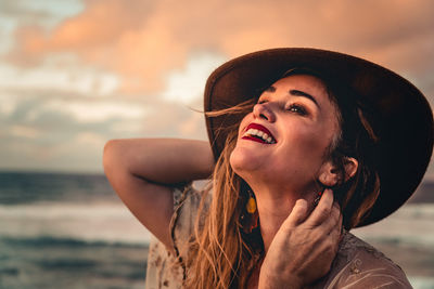 Portrait of smiling young woman looking away at beach against sky