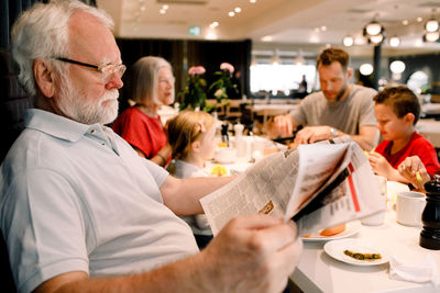 Senior man reading newspaper while sitting family in restaurant during breakfast