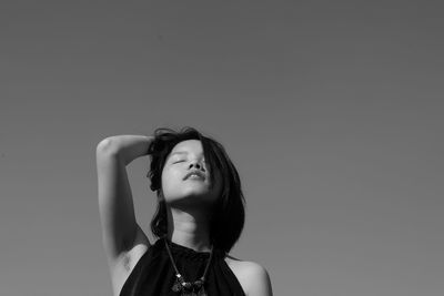 Young woman with hand in hair against clear sky