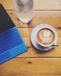 High angle view of cappuccino by blue laptop on table