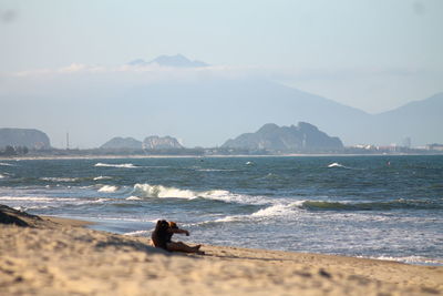 Scenic view of people sitting at sea against sky