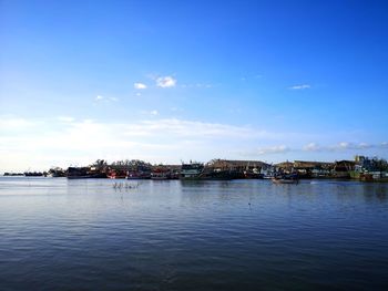 Scenic view of river by buildings against blue sky