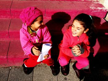 High angle view of siblings sitting on steps during sunny day