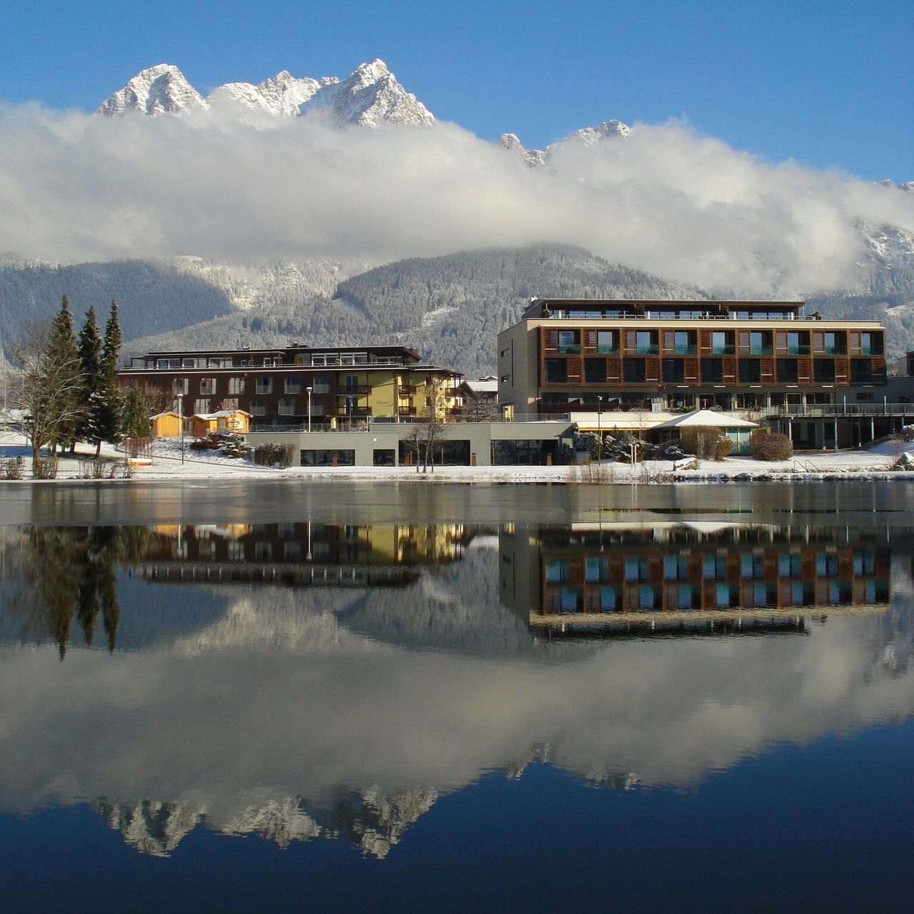 mountain, mountain range, winter, snow, cold temperature, architecture, building exterior, built structure, sky, reflection, season, cloud - sky, lake, house, snowcapped mountain, nature, scenics, beauty in nature, tranquility, tranquil scene