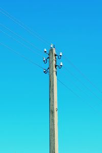 Low angle view of electricity pylon against clear blue sky