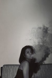 Side view portrait of young woman smoking against wall