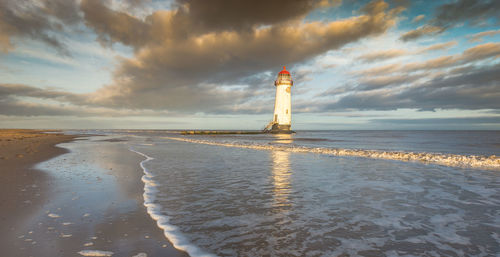 Lighthouse amidst sea and buildings against sky