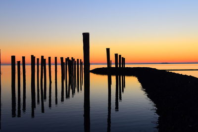 Wooden posts in lake against clear sky during sunset