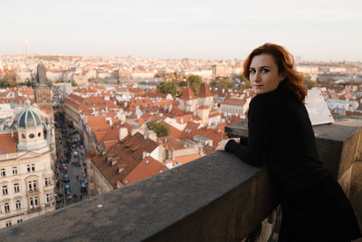 Portrait of young woman with townscape against sky in city