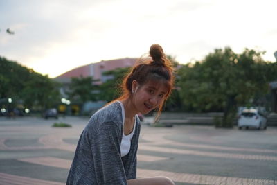 Portrait of smiling young woman on road against sky during sunset