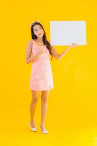 Portrait of a smiling young woman standing against yellow background