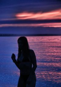 Silhouette woman standing on beach against sky during sunset