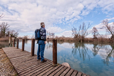 Hiker standing on jetty by lake against sky