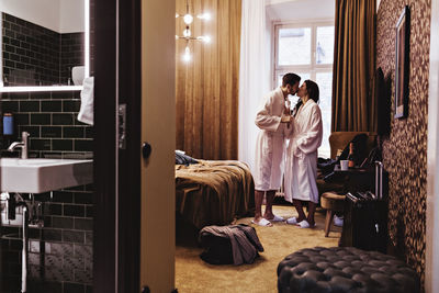 Couple kissing while holding champagne flutes by bed in hotel room