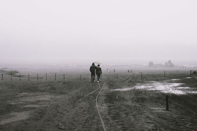 Rear view of men walking on snow covered field against sky