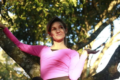 Low angle view of woman looking away while leaning on tree trunk