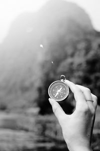 Cropped hand holding navigational compass against mountains
