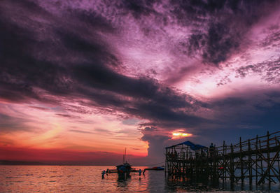 Silhouette of boats in sea against cloudy sky