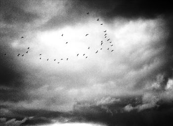 Low angle view of birds flying against cloudy sky