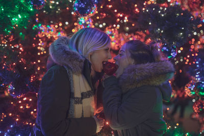 Female friends eating caramelized apple during christmas at night