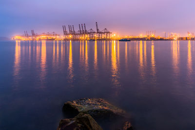 Illuminated commercial dock by sea against sky at night