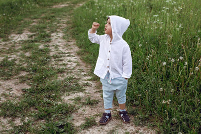 Boy child in a green field in summer in a white shirt with a hood made  linen in shorts and sandals