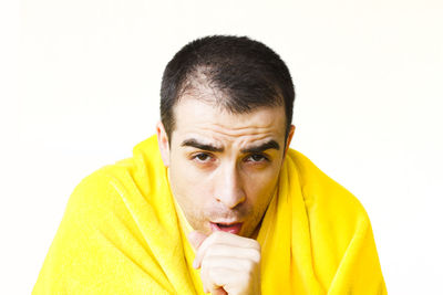 Portrait of man covered with yellow blanket against white background