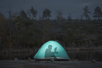 A man in a lighted tent is reading a book. far away from civilization. themes of  outdoor activities