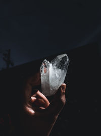 Cropped hand holding condom while standing against black background