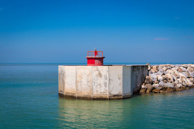 Lighthouse by sea against blue sky