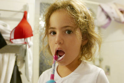 Portrait of cute girl brushing teeth while standing at home