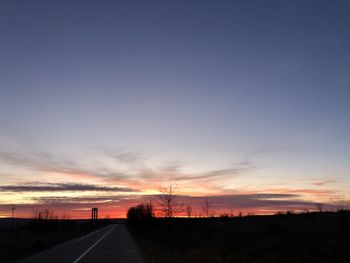 Road amidst silhouette landscape against sky during sunset