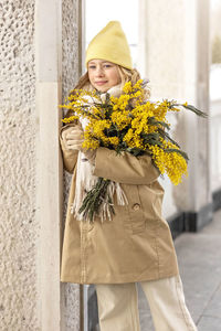  a girl in a beige coat with a bouquet of mimosa in her hands in the park.international women's day 