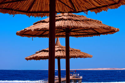 Parasols by sea against clear blue sky