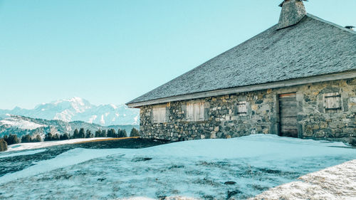 Snow covered houses by mountain against clear sky