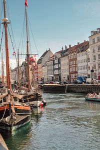 Sailboats moored on canal in city against clear sky