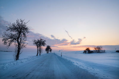 Scenic view of snow covered road against sky during sunset