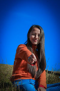 Young woman using smart phone on field against blue sky