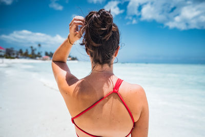 Rear view of woman in bikini at beach against sky