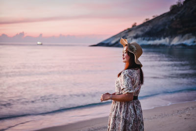 Woman standing at beach against sky during sunset