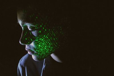 Close-up of shirtless woman with illuminated green lights against black background