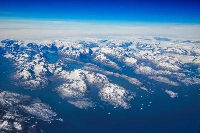 Aerial view of snowcapped mountains against blue sky