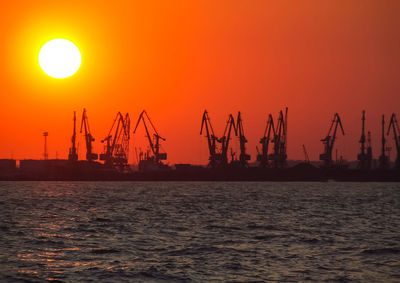 Silhouette cranes at commercial dock against sky during sunset