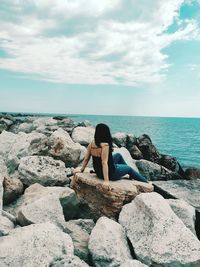 Woman sitting on rock by sea against sky