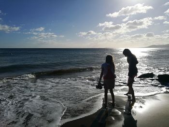 Friends standing on beach against sky during sunset