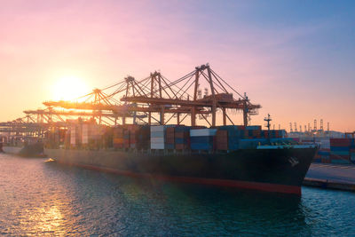 Cranes at commercial dock against sky during sunset