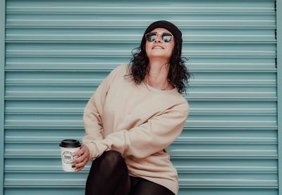 Young woman wearing sunglasses standing against wall