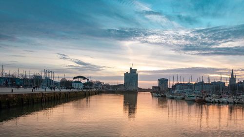 River by buildings in city against sky at sunset